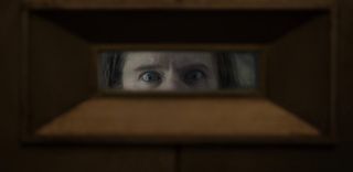 A pair of piercing blue eyes appears in a vault door window