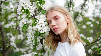 Blond haired young woman among white blossoms - stock photo