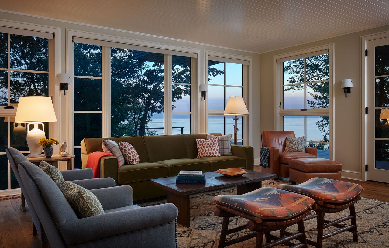living room at dusk with large windows overlooking the lake green sofa blue armchairs and two kilim stools