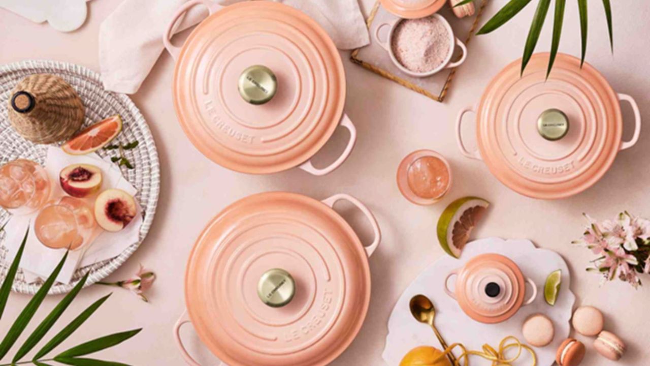 Some of Le Creuset&#039;s stoneware and cast iron pots in their new colorway, peche on a table with other peach colored food and glass