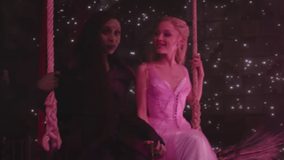 Elphaba and Glinda on a swing together with star projections around them and pink lighting in Wicked For Good