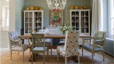 light blue painted dining room with large white cabinets, white flower shaped ceiling light, wooden table and mismatched wooden and floral chairs