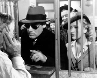 a man in a hat and sunglasses speaks to a bank teller in the movie arsenic and old lace