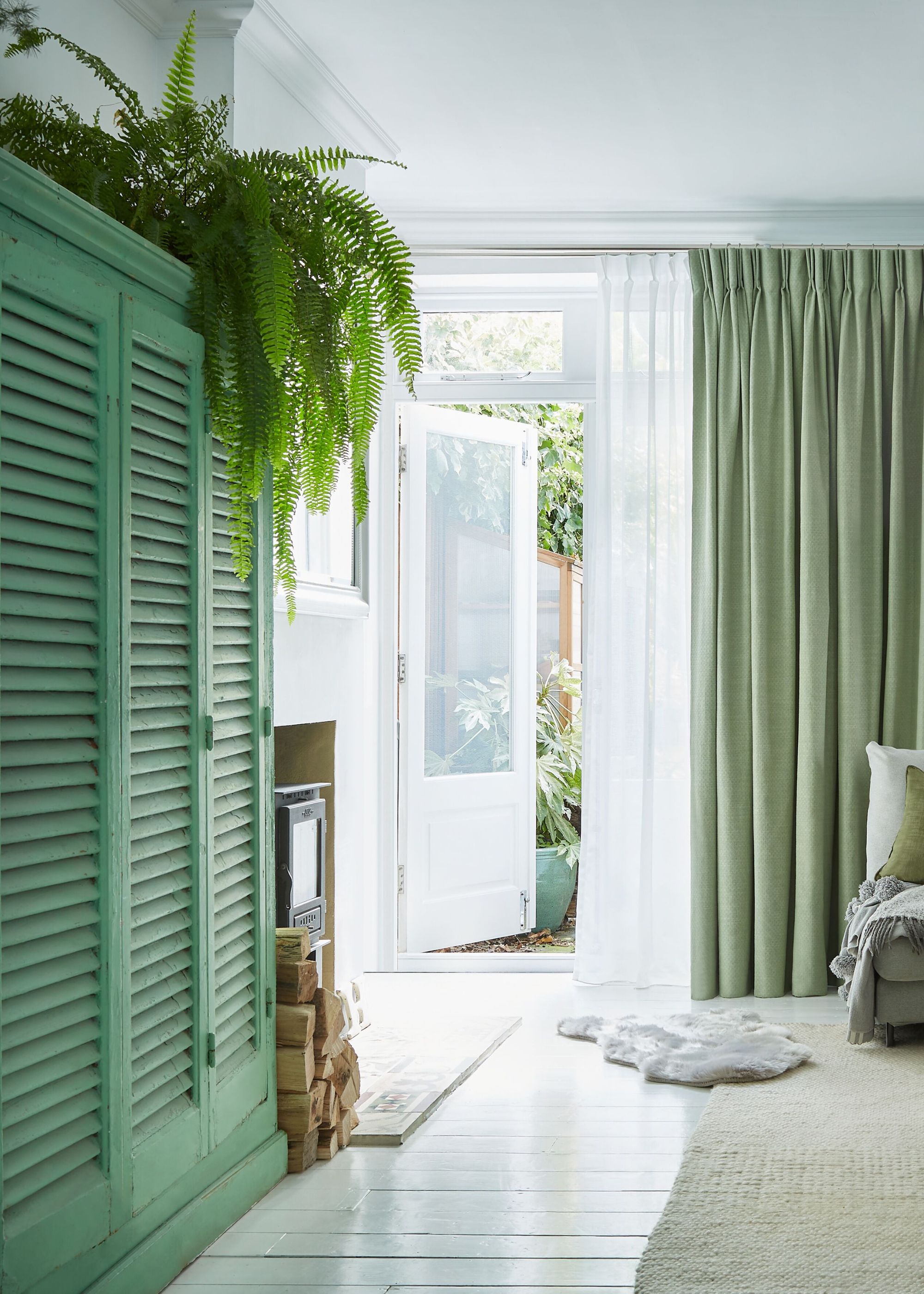 A living room with French doors with sheer curtains layered with green drapes.