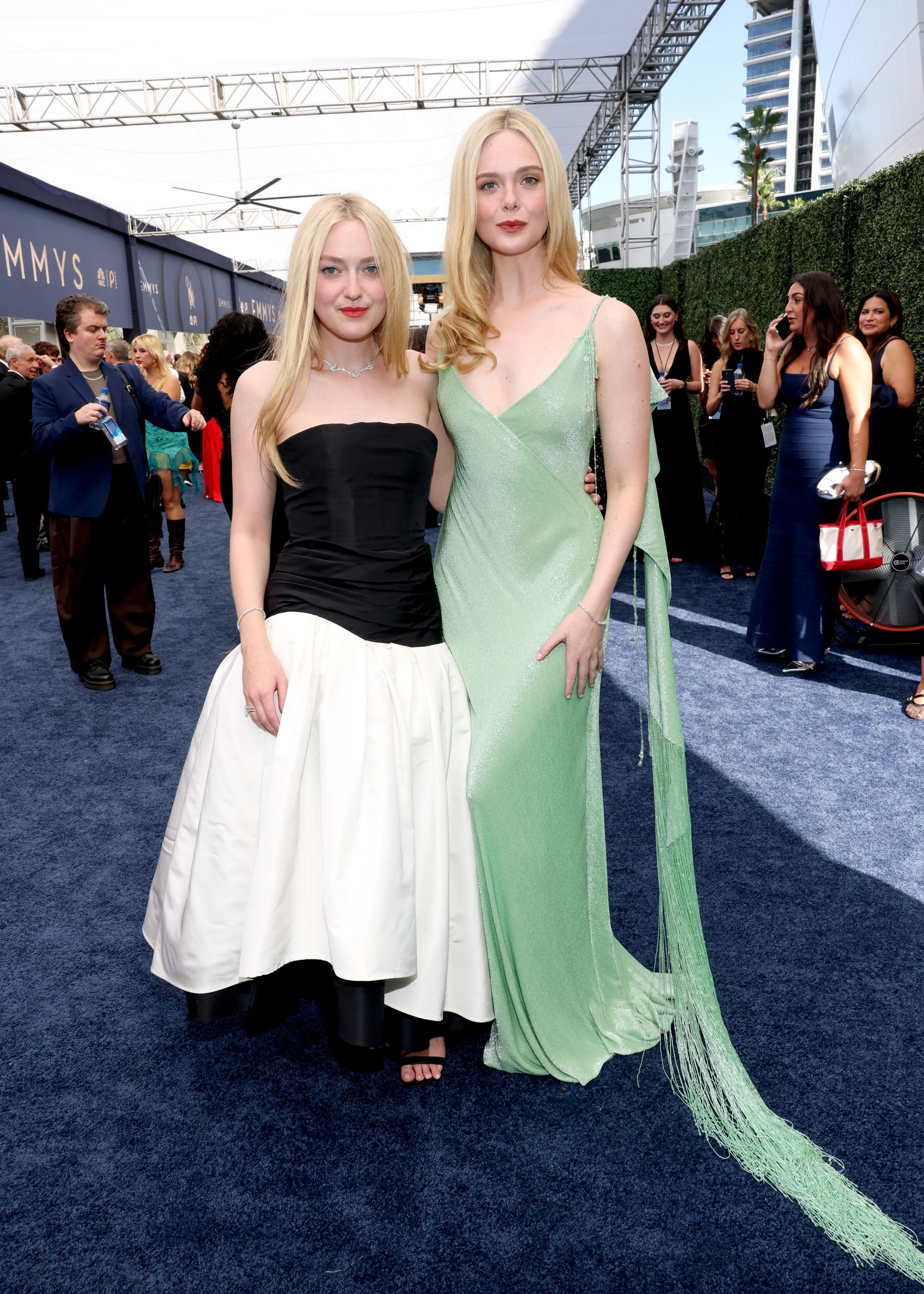 two blonde women on a blue carpet, one in a black and white gown, the other in a mint green gown