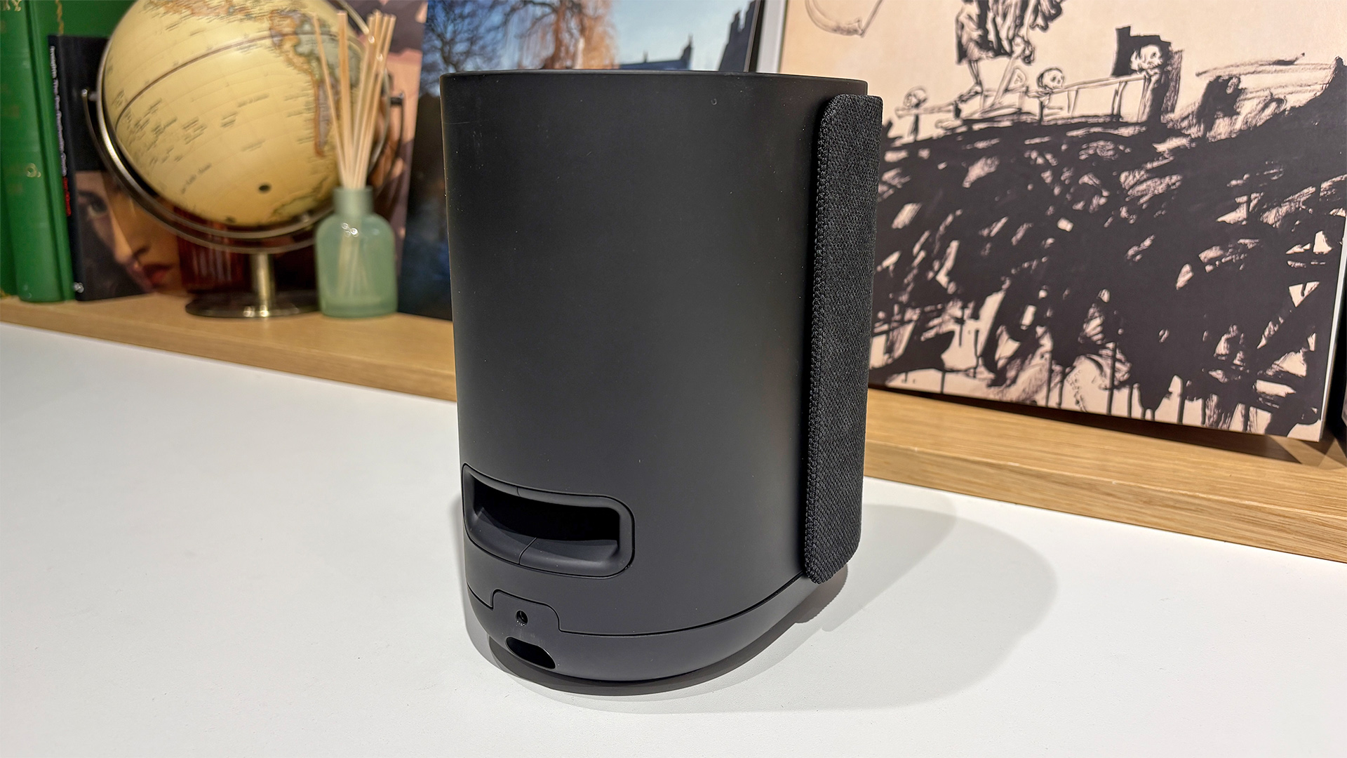 Rear port of Bose Lifestyle Ultra Speaker wireless speaker on white surface in front of busy bookshelf