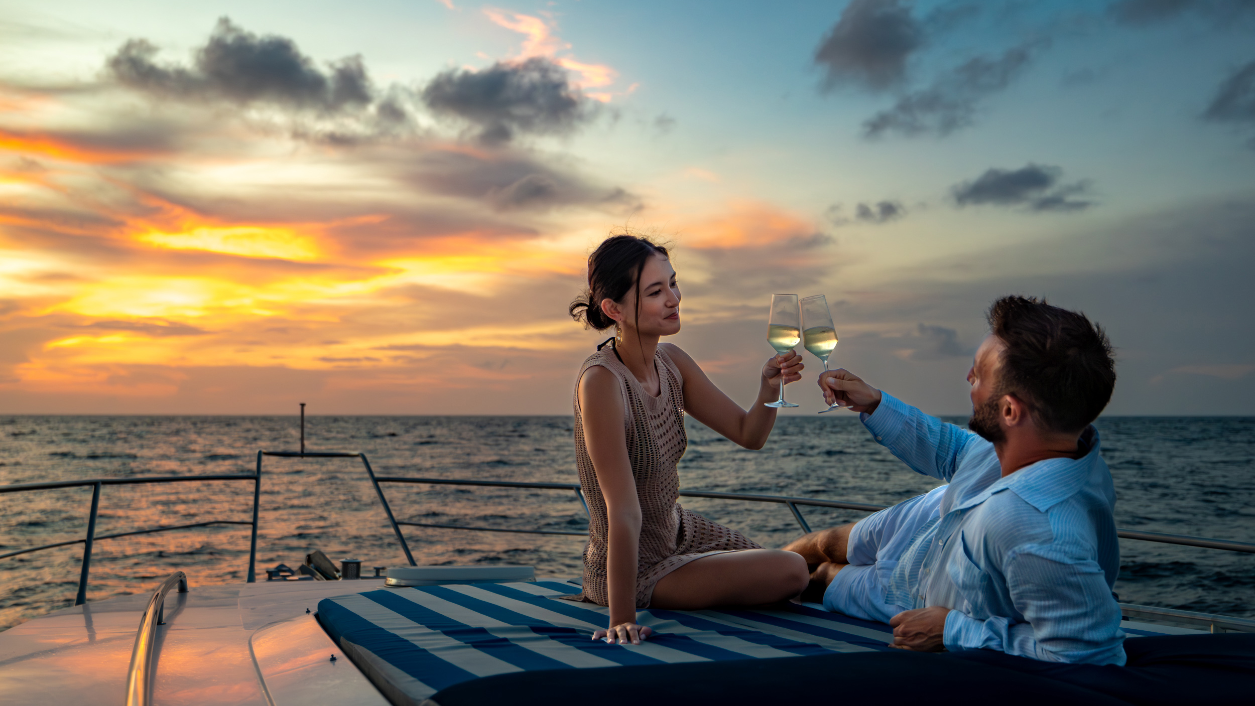 A couple on a boat at sunset, raising glasses of white wine to each other