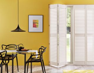 White wooden door window shutters in yellow dining area of kitchen with artwork on walls
