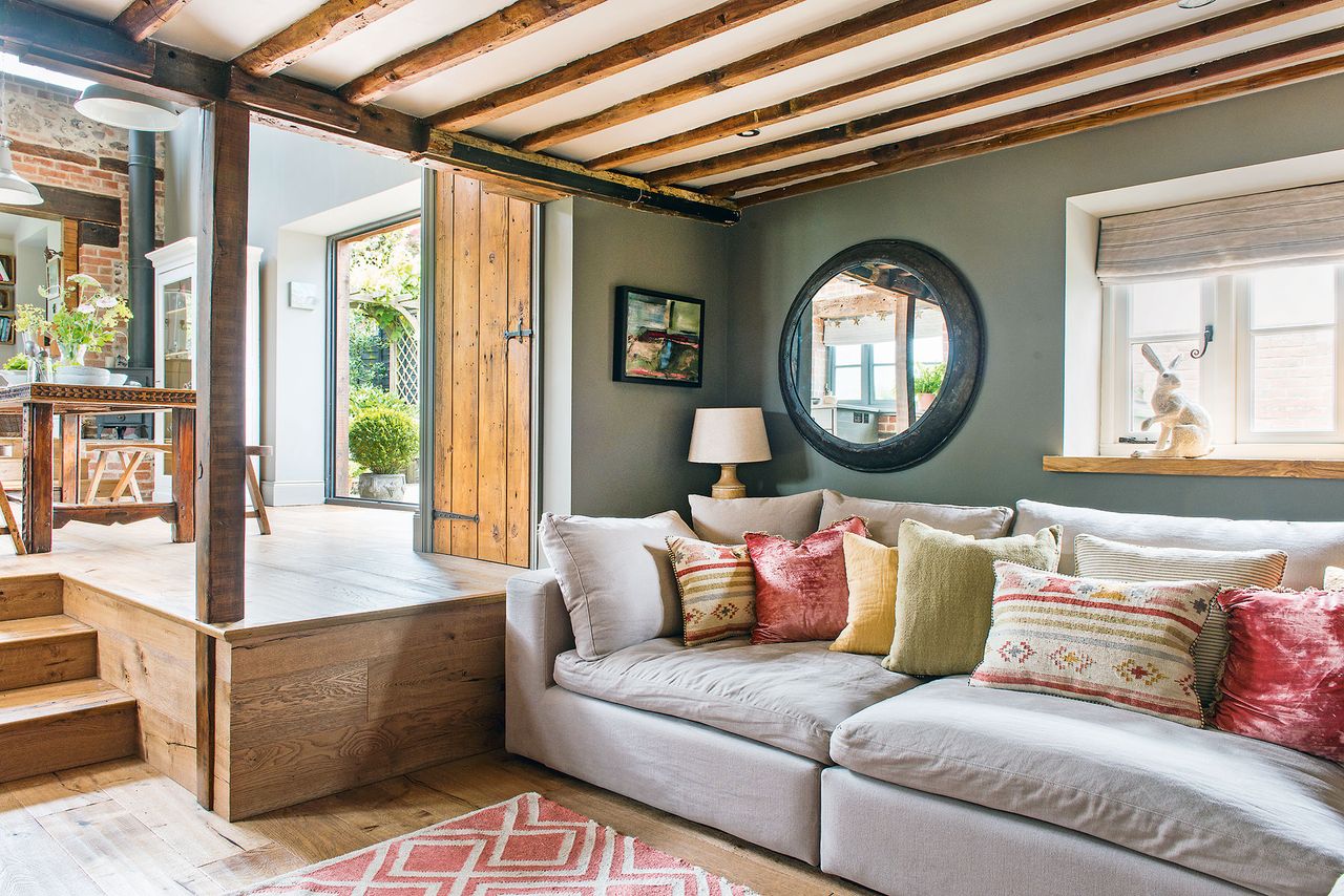 living room with green walls and beams pale gray sofa bright cushions and view to kitchen up steps