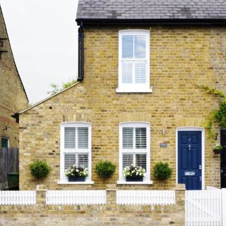 house exterior with yellow brick wall white windows blue door and plants