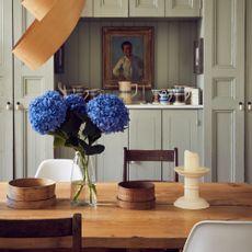 A dining room with a vase of hydrangeas on the table with a vintage painting hung on the back wall