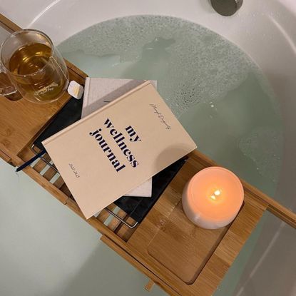 papier wellness journal, candle and cup of tea on a table over a bathtub