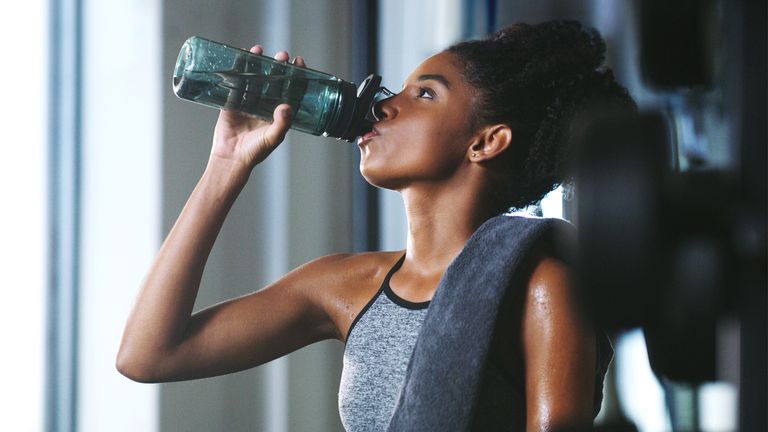 woman drinking out of her water bottle at the gym
