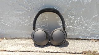 The 1More SonoFlow noise-cancelling headphones rested up against a concrete wall
