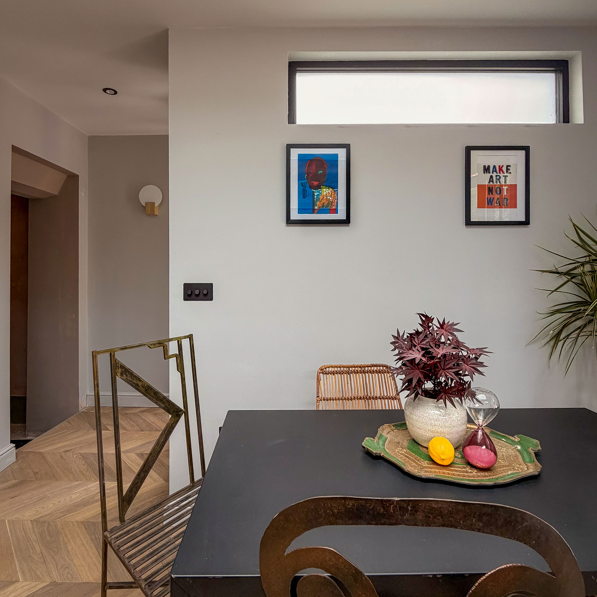 White dining space with high window, two prints on wall, black table and mismatched dining chairs