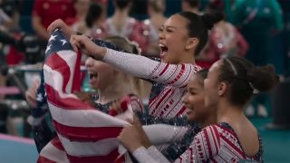 The U.S. Olympics gymnast women, including Simone Biles, celebrate with the flag after team victory.