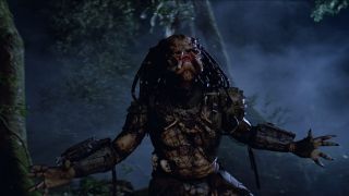 Still from the movie Predator. Here we see Predator without most of their armor, throwing their head and arms back in a battle cry. Image for Predator movies ranked article.