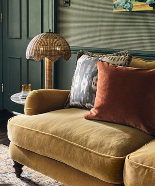 Scalloped table lamp on side table next to yellow velvet sofa with dark walls