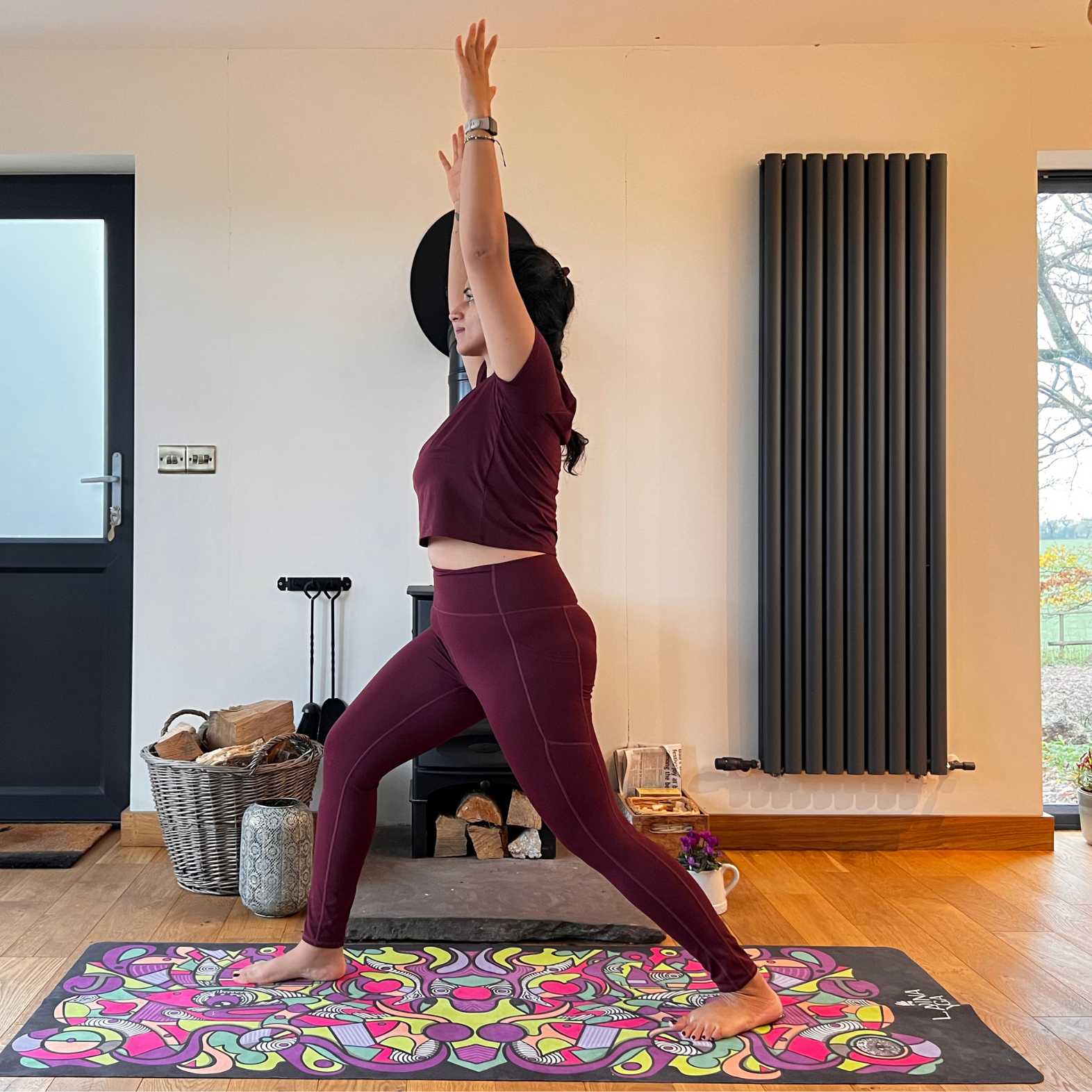 Maysun Hassanaly stands on a yoga mat performing revolved warrior. She is in a lunge position, with her right foot forward, right knee bent and left leg extended behind. Her arms are extended overhead and she is facing forward.