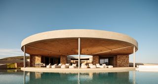 Exterior shot of a circular Greek home with infinity pool and sun loungers