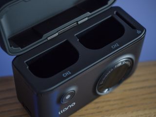 The Llano Dual Camera Battery and Charger set on a wooden surface against a purple background