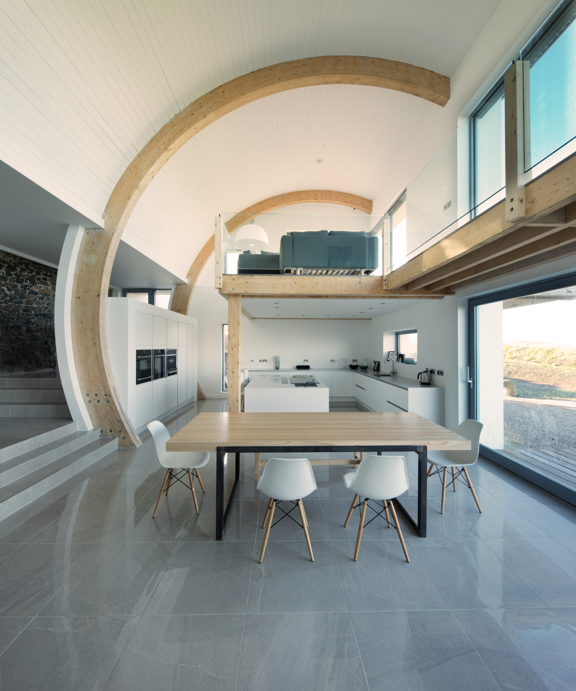 inside of kitchen extension with curved roof, curved oak modern beam, grey tiled floor, large patio doors and mezzanine level above kitchen