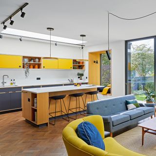 open plan kitchen and living area with island and breakfast bar and stools yellow cabinetry and a sofa