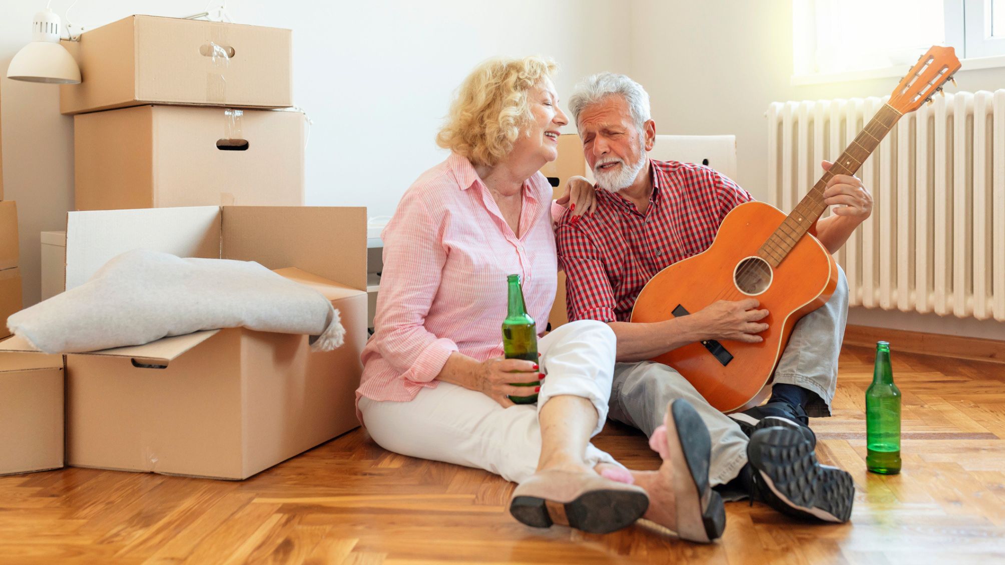 A couple singing together while the man plays guitar as they take a break from moving into their new home. 