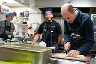 SUNBURY, ENGLAND - APRIL 18: Prince William, Prince of Wales speaks with head chef Mario Confait, (C) as he cuts celery while helping to make a bolognese sauce during a visit to Surplus to Supper, in Sunbury-on-Thames on April 18, 2024 in Surrey, England. The Prince visited Surplus to Supper, a surplus food redistribution charity, to learn about its work bridging the gap between food waste and food poverty across Surrey and West London. (Photo by Alastair Grant-WPA Pool/Getty Images)