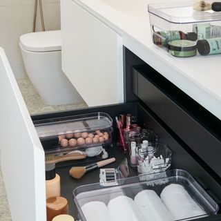 Bathroom sink drawer storing makeup and toiletries in clear boxes