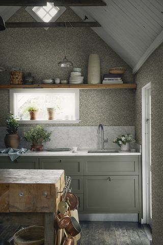 sage green kitchen cabientry and patterned wallpaper. Marble splashback and worktops with reclaimed vutchers block and open wooden shelves displaying pots and ceramics