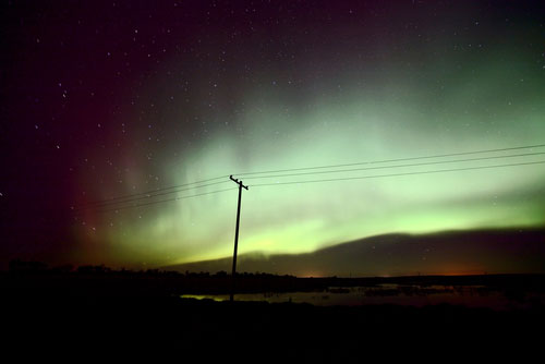 lonely power line silhouetted against aurora in sky