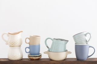 A selection of mugs and ceramic jugs on display on a wooden shelf.