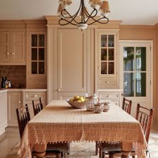 Dusty pink kitchen with chandelier and tablecloth, wooden chairs