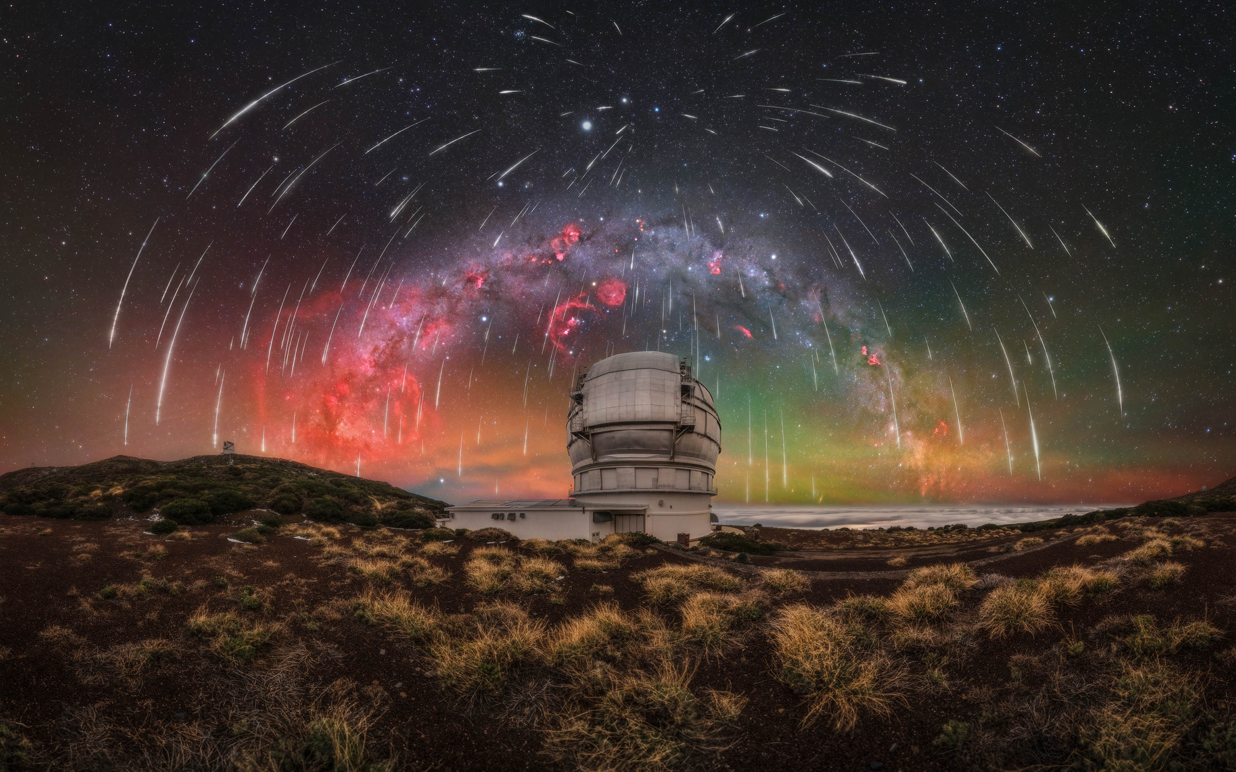 Observatory under a meteor shower with a colorful Milky Way arching across a starry night sky