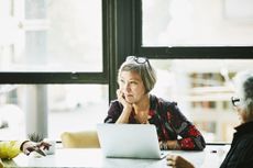 An older woman with an open laptop sits in a meeting.