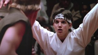 Ralph Macchio stands with his arms posed in the middle of a karate match in The Karate Kid.