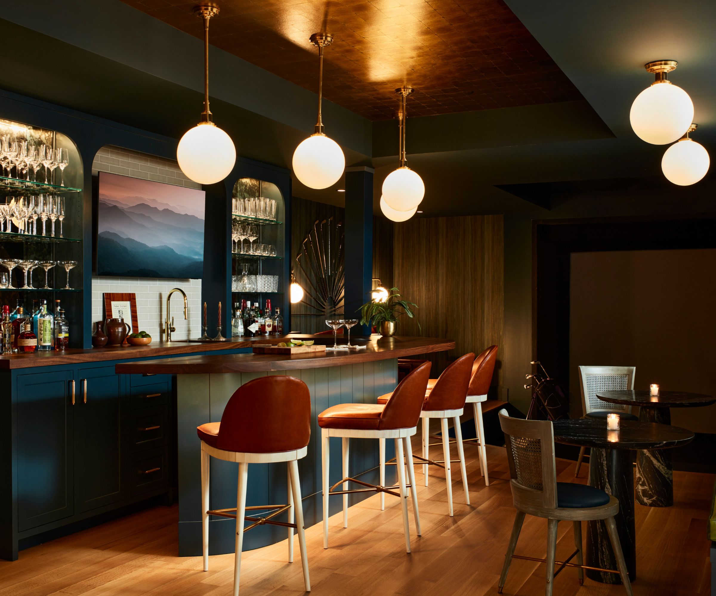 basement home bar with dark navy walls, copper ceiling, large white globe ceiling lights, leather bar stools