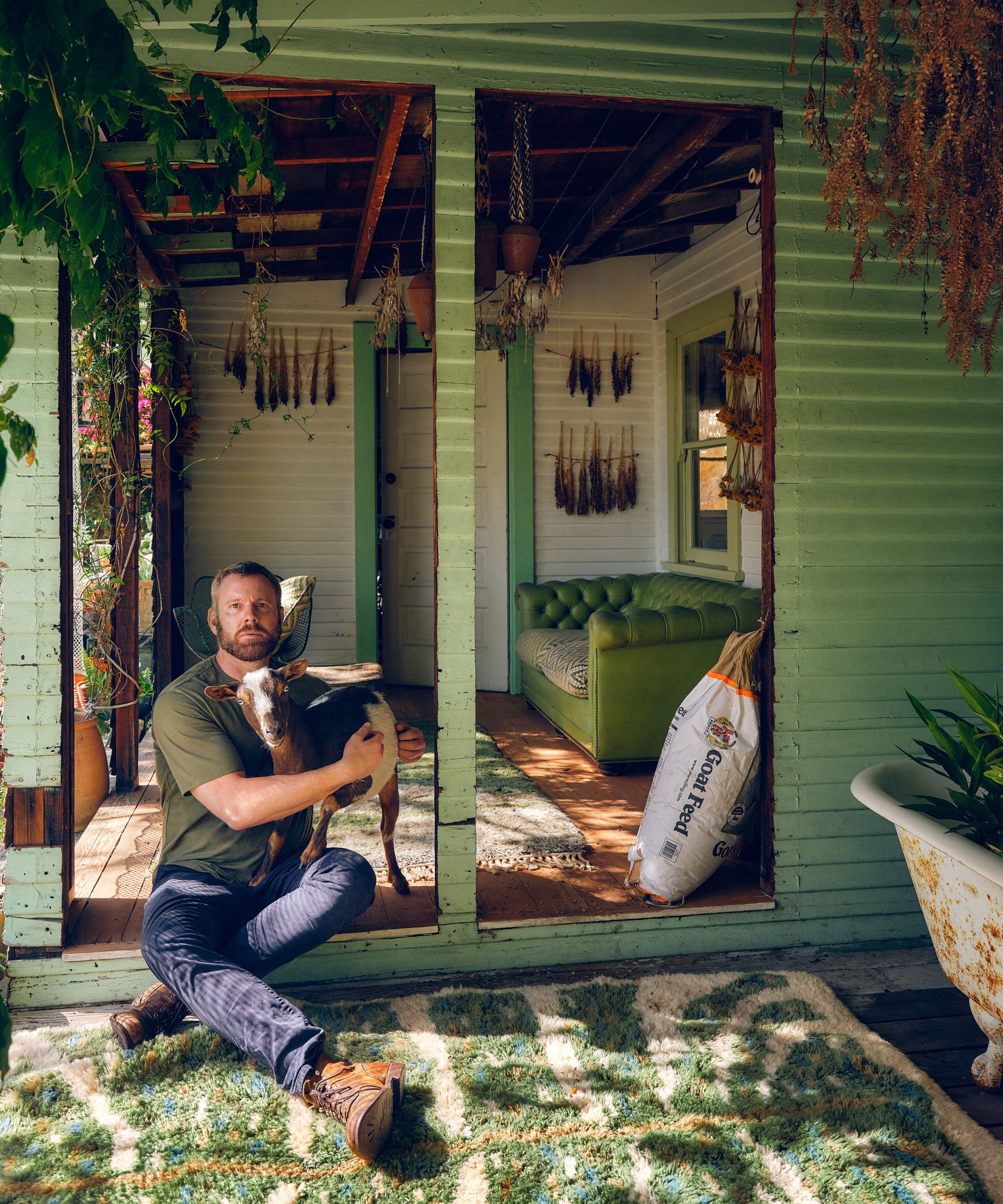 Richard Christiansen sitting with his goat in a green wooden doorway at home
