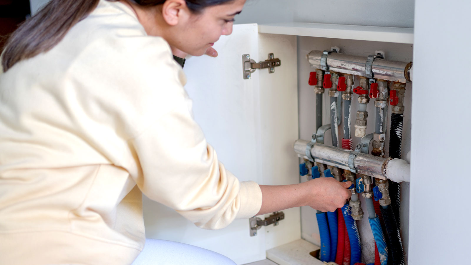 Woman switching off underfloor heating pipes in cupboard