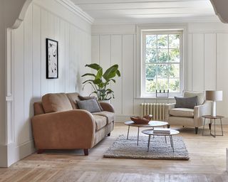 Mid-brown sofa with splay foot and neutral armchair in room with paneled walls