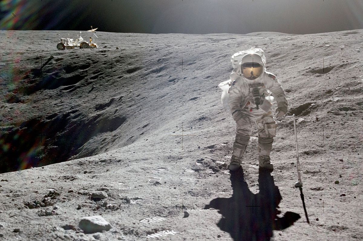 Apollo 16 lunar module pilot stands at the rim of Plum crater with the lunar rover parked in the distance on April 21, 1972.