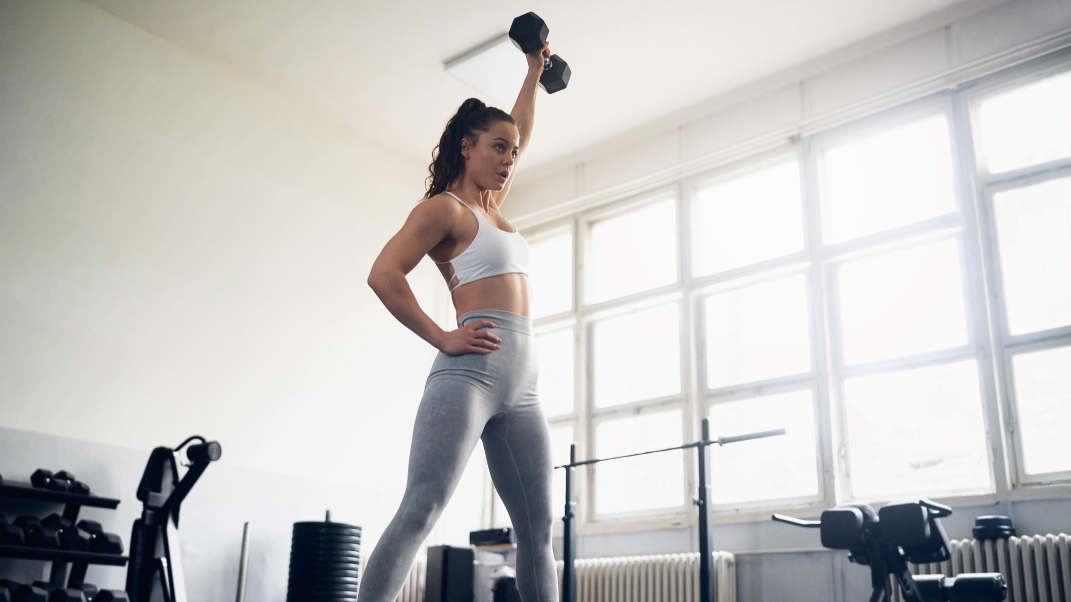Woman exercising in a gym, holding one dumbbell overhead