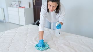 A woman scrubbing a mattress with a cloth in one hand a spray bottle in the other