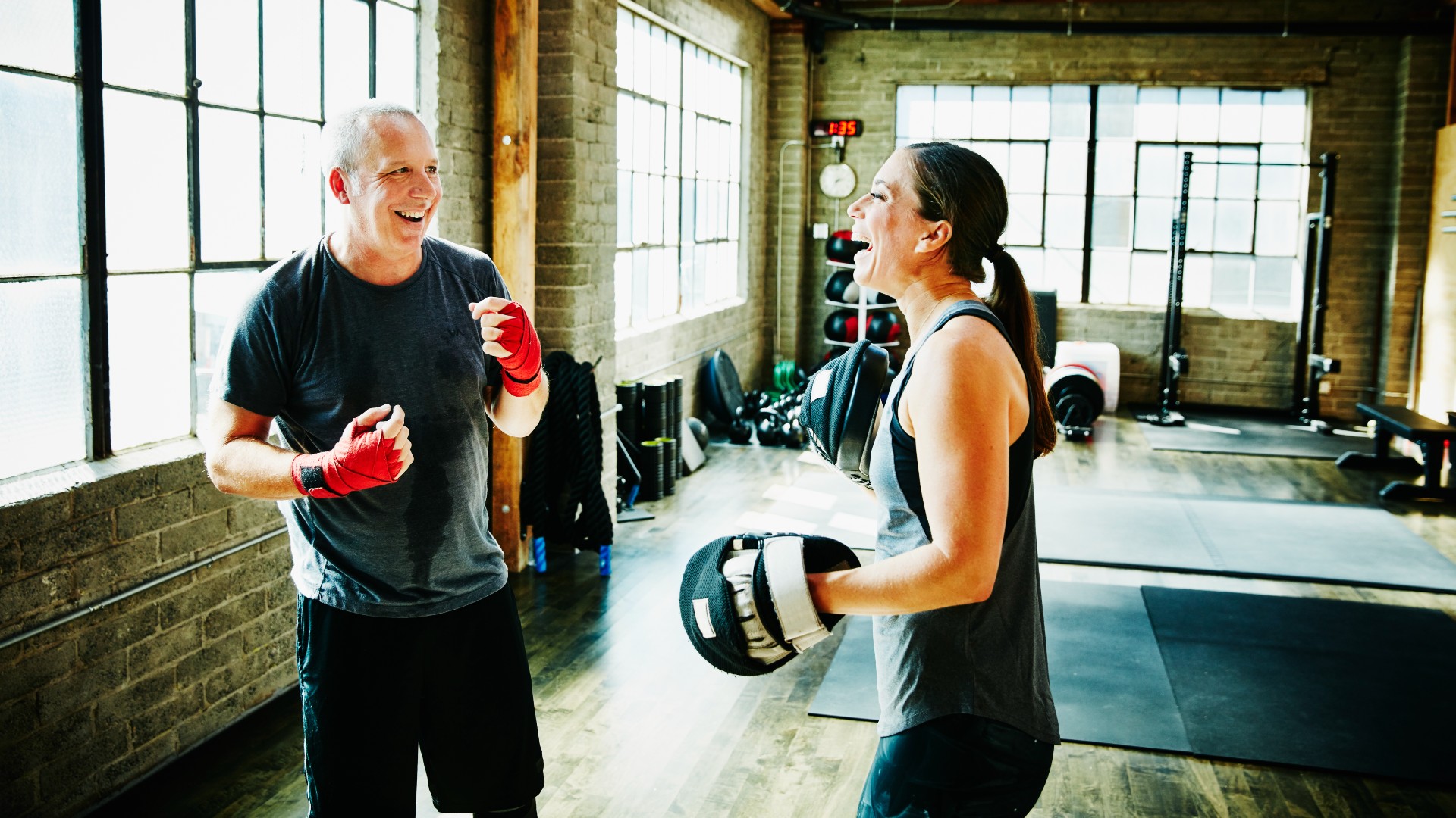 Mature athlete and coach laughing during boxing training session in gym