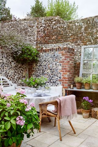 backyard with table and chairs and pink throw with flint walls around and potted plants and a window-frame mirror
