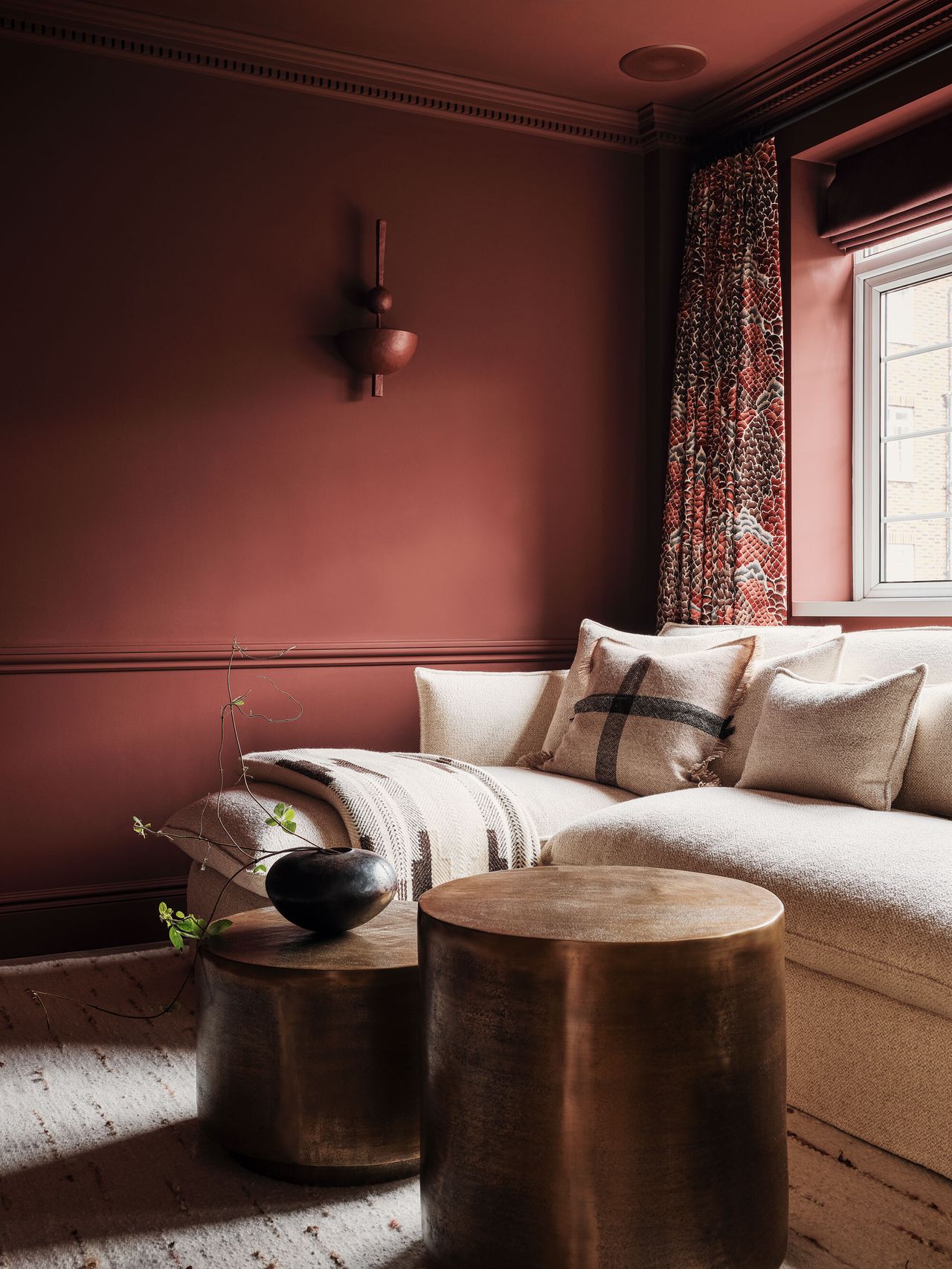 A white corner sofa in a living space with red painted walls and patterned curtains