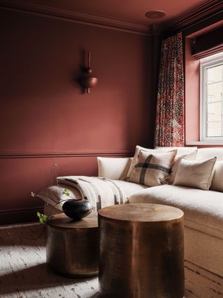 A white corner sofa in a living space with red painted walls and patterned curtains