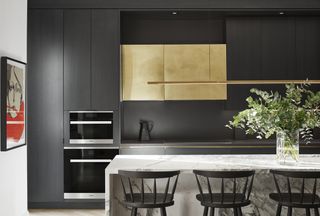 A black painted kitchen with a gold cabinet and a marble island