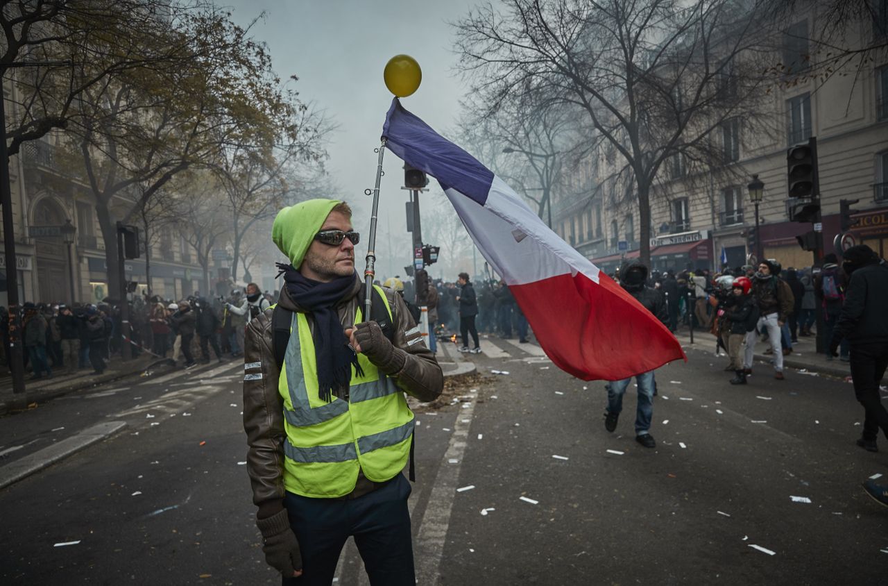 PARIS, FRANCE - DECEMBER 05: A Gilet Jaune, or Yellow Vest&amp;#039; holds a French Tricolor amidst tear gas as protestors and French Riot Police clash during a rally near Place de Republique in suppo